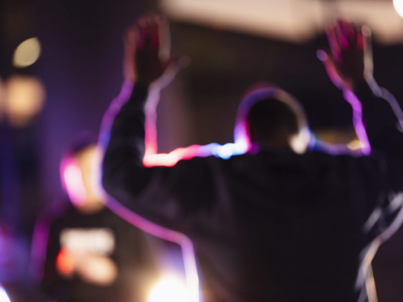 A man with his hands raised, surrendering to police at night. His back is to the camera. A policewoman is standing in the background facing the suspect.